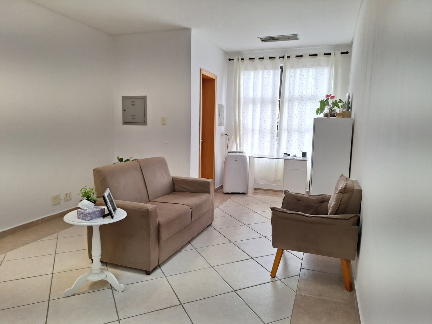 Sala de atendimento com sofá, poltrona e cortinas claras